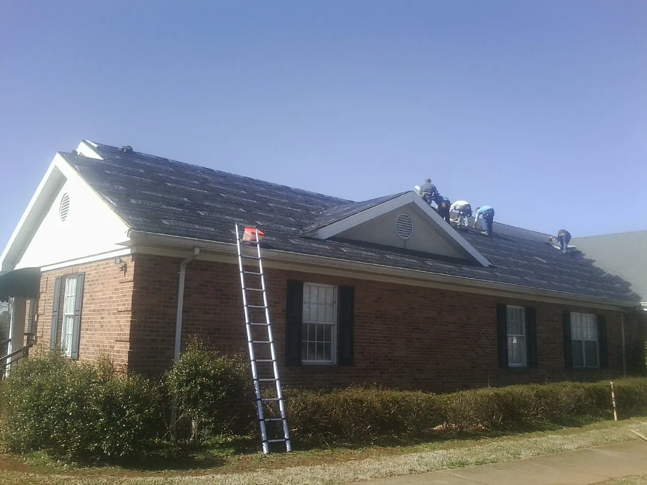 Crew tearing shingles off a brick ranch roof with a ladder set — Metal Roof Repair work by our crew in Tazewell