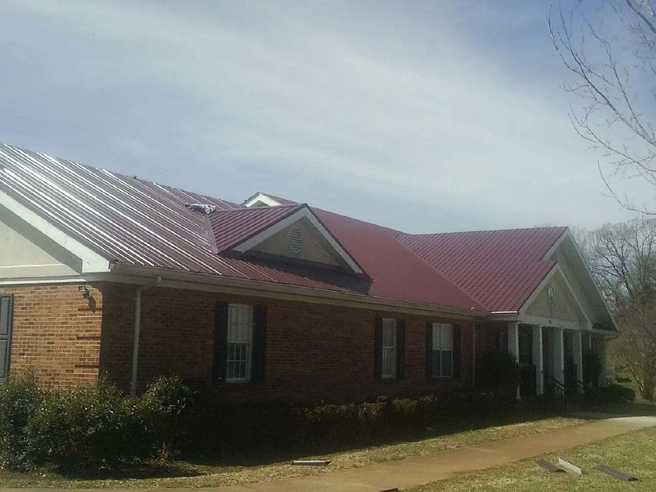Red metal roof with gabled entries on a long brick building, from a Hail Damage Roof Repair job in Tazewell