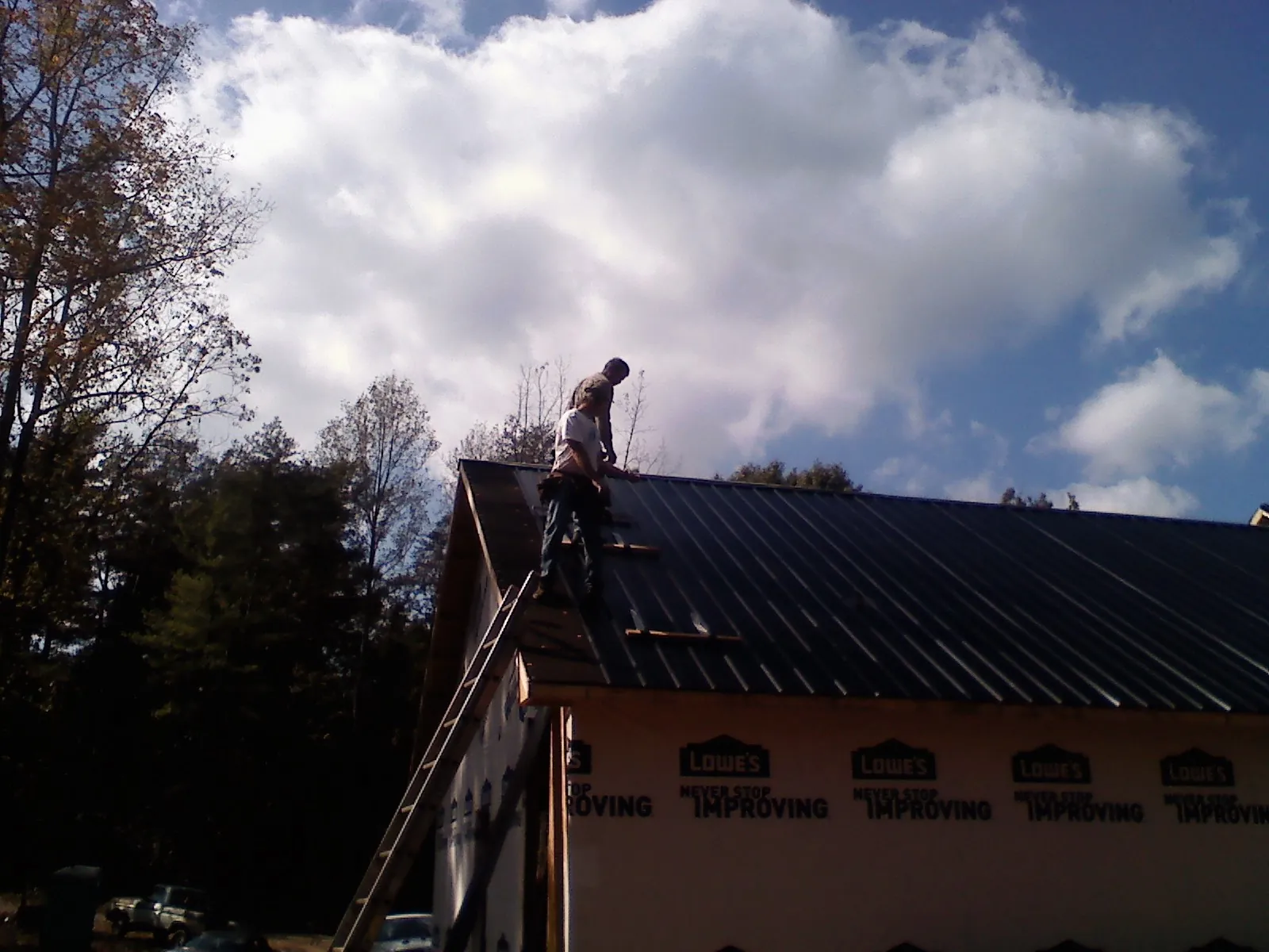 Roofer fastening dark metal panels high against a cloudy sky, from a Roof Inspection job in Tazewell