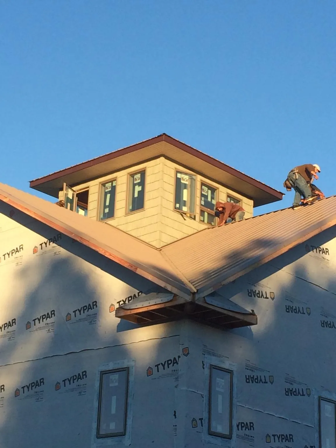 Roofers working around a rooftop cupola on a new metal roof at sunset in Tazewell